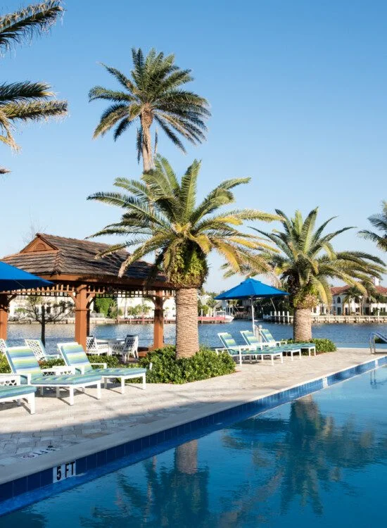 resort-style, waterfront outdoor swimming pool lined with palm trees and lounge chairs at Harbour's Edge Senior Living Community