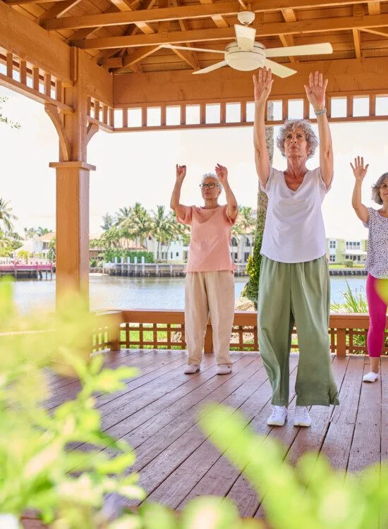 group of three senior women practice Tai Chi in an outdoor gazebo on a sunny day by the water at Harbour's Edge Senior Living Community