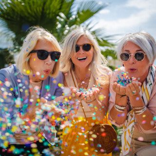 Fashionable mature friends having fun and celebrating by blowing colorful confetti in city street