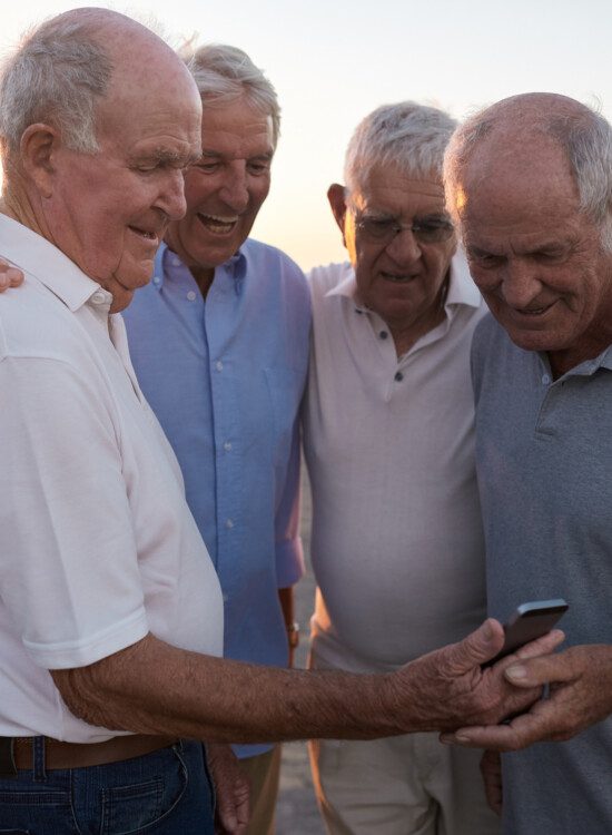 group of four senior men laugh while looking at a phone screen together