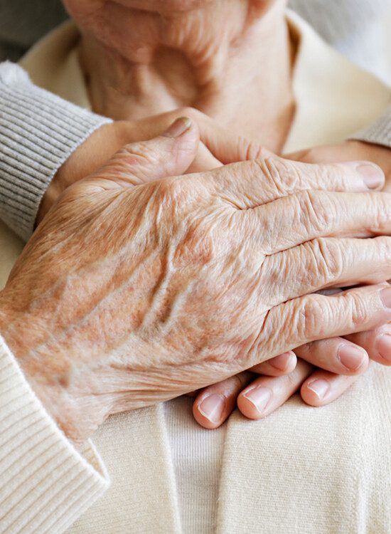 close-up of senior with their adult child embracing them from behind, arms around the neck