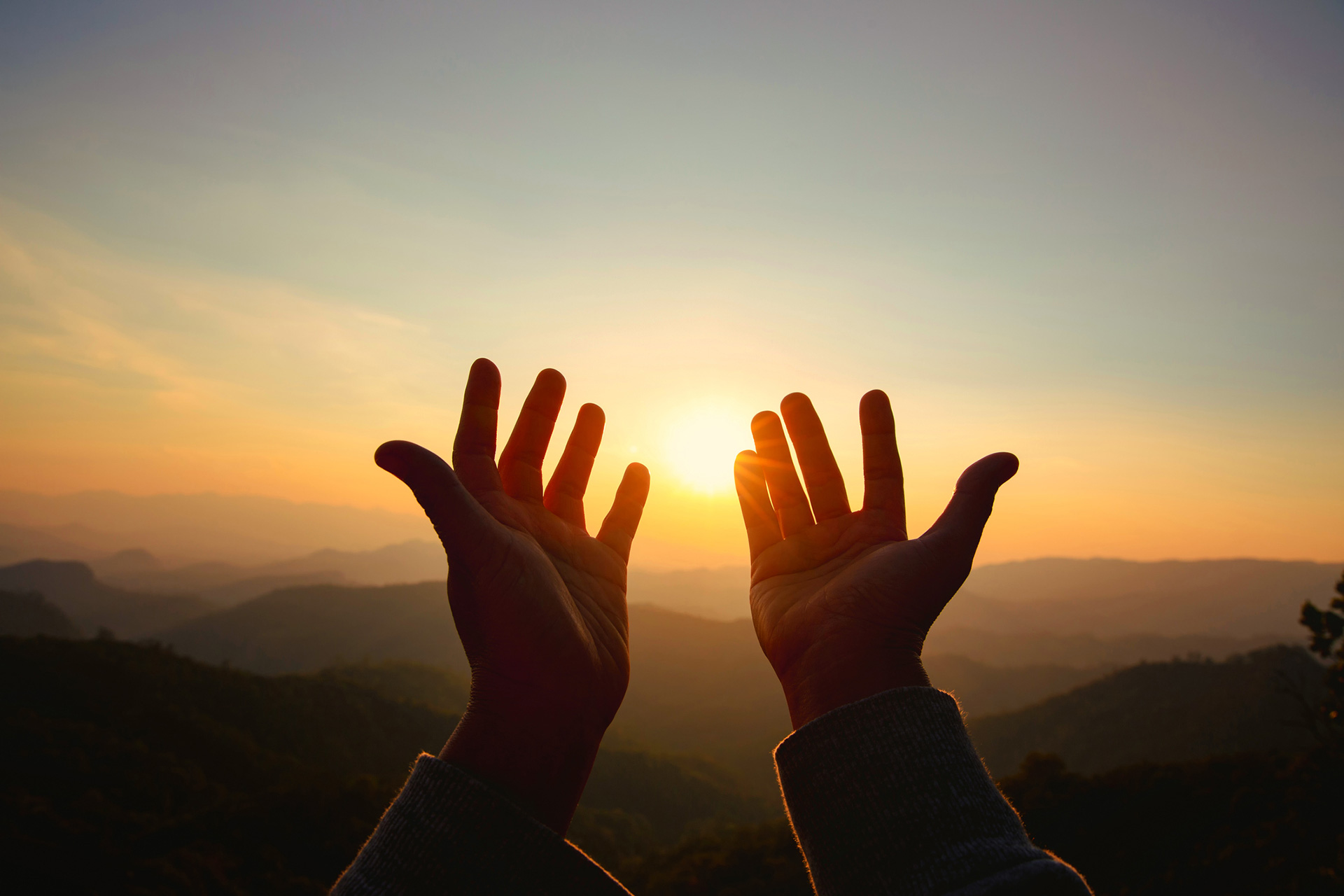 open hands reaching towards the sunset in the mountains