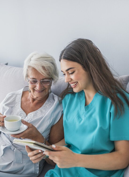 senior woman drinking coffee on her bed is shown information by her caretaker while seated