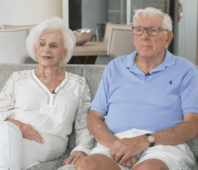 Senior couple seated on comfortable couch in their apartment for an interview