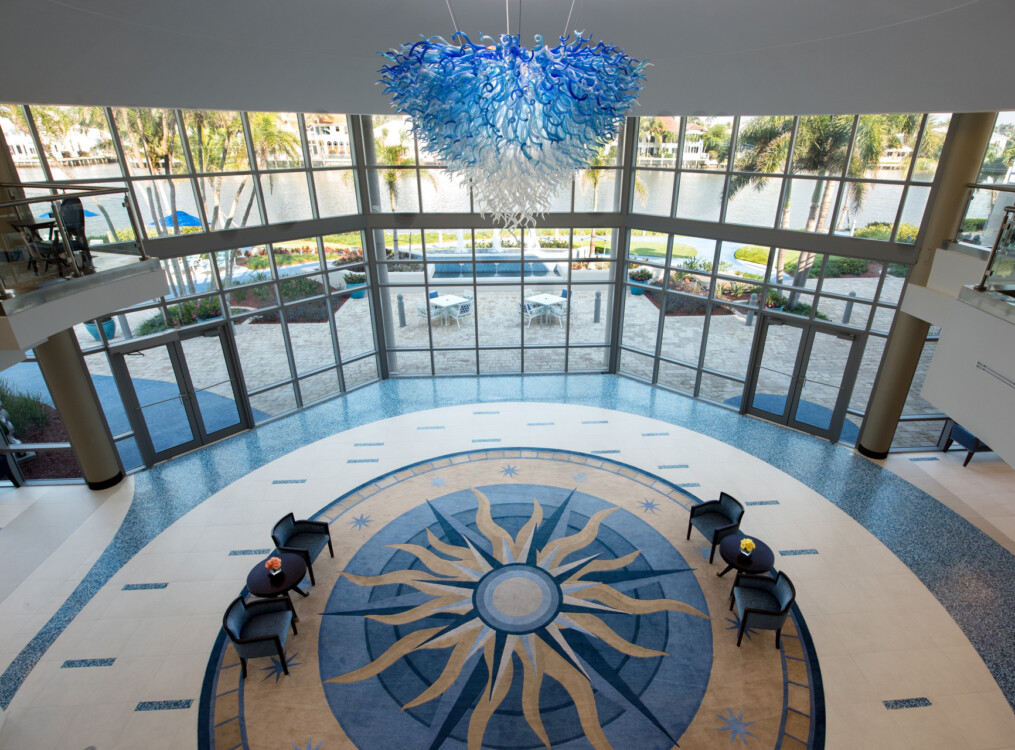 blue and white glass chandelier hanging from the ceiling at Harbour's Edge, backdropped by floor-to-ceiling windows showing outdoor lounge