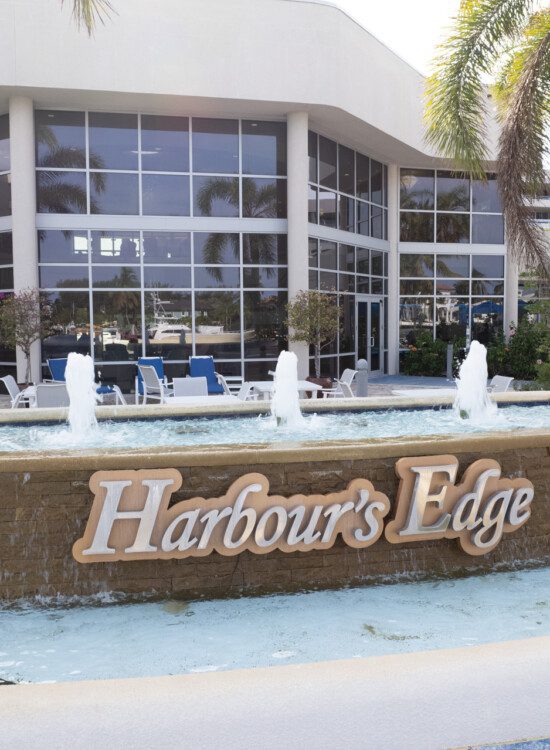 beautiful fountain with the community name and palm trees outside of a lounge area at Harbour's Edge Senior Living Community