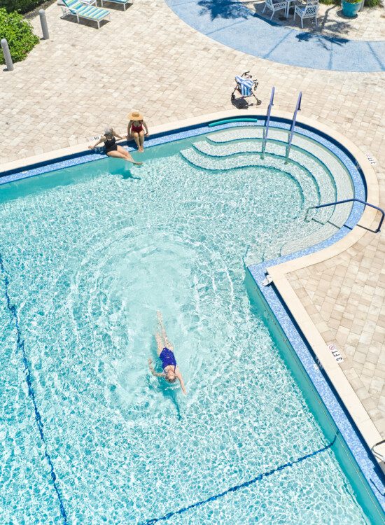 aerial view of seniors swimming in resort-style outdoor pool at Harbour's Edge Senior Living Community, featuring tables and lounge area