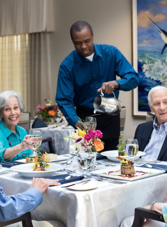 group of seniors smile while being served dessert and wine during an upscale meal together at their senior living community