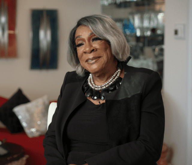 well-dressed senior woman (Dr. Barbara Shuler) smiles while seated for an interview