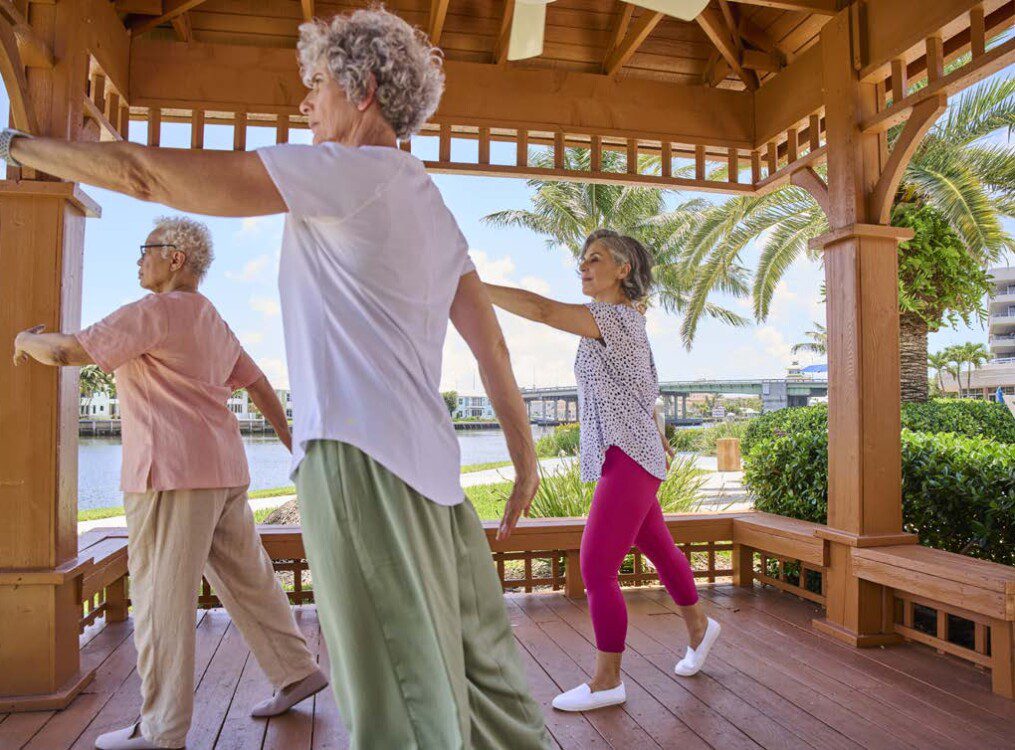group of senior women practice Tai Chi in an outdoor gazebo on a sunny day by the water at Harbour's Edge Senior Living Community