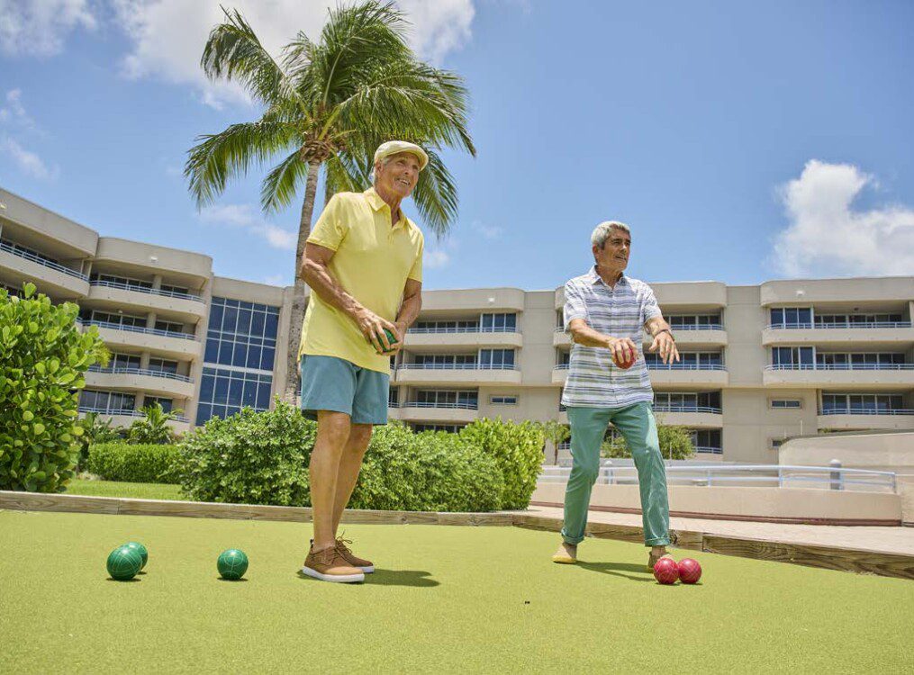 two smiling senior men play bocce ball in the sunny courtyard at Harbour's Edge Senior Living Community