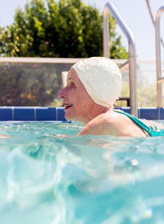 side profile of senior woman in white swimming cap doing laps in the outdoor pool at Harbour's Edge Senior Living Community