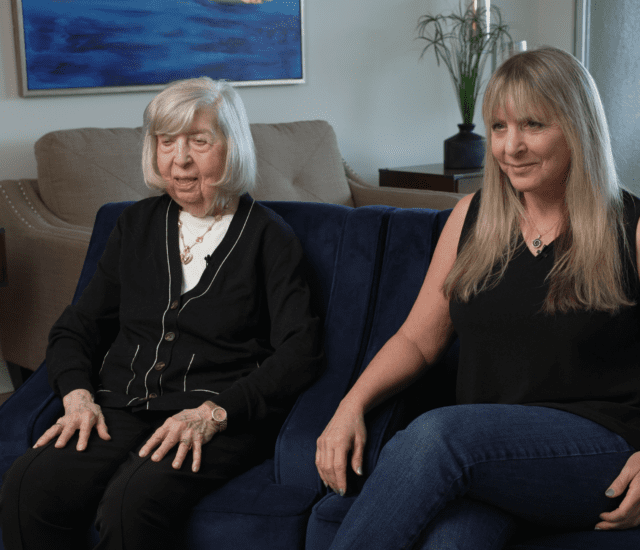 senior woman and her daughter sit on black chairs side-by-side for an interview