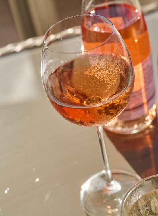 close-up of long-stemmed wine glasses filled with pink wine, sparkling in the sun