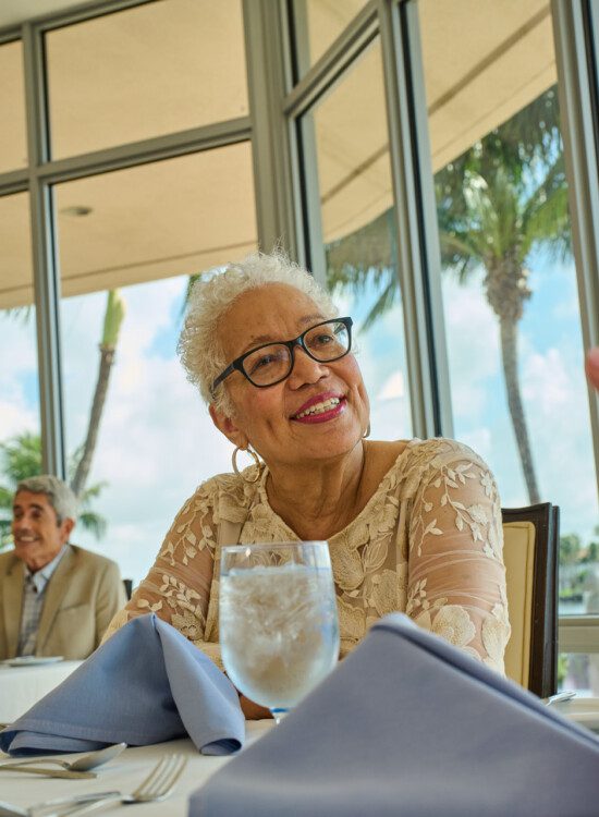 stylish senior woman in glasses smiles at her companions while dining at the upscale venue at Harbour's Edge Senior Living Community