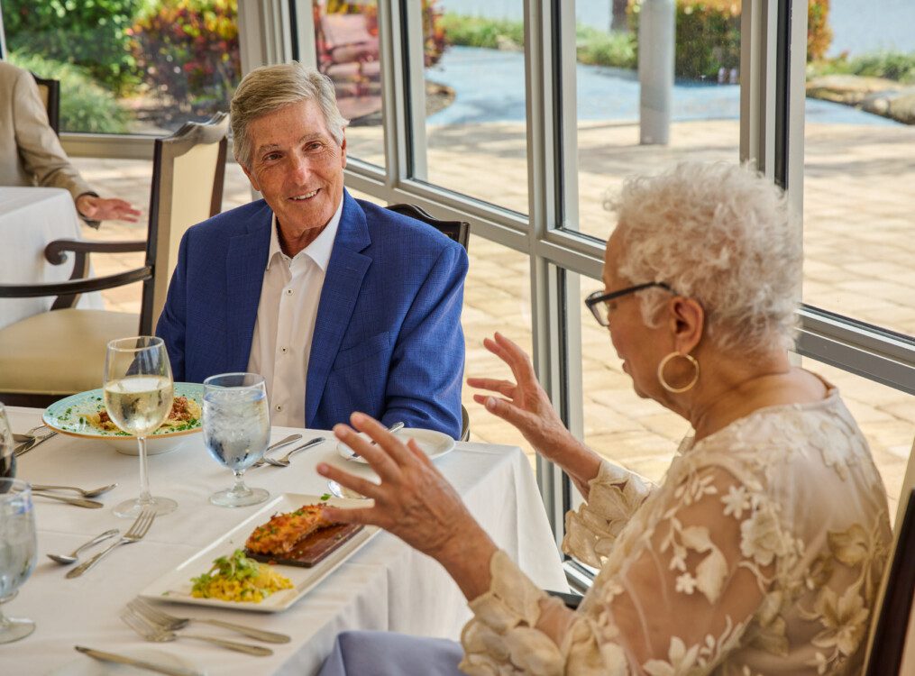 smiling senior friends enjoy wine and dinner at the upscale dining room at Harbour's Edge, with panoramic waterfront views