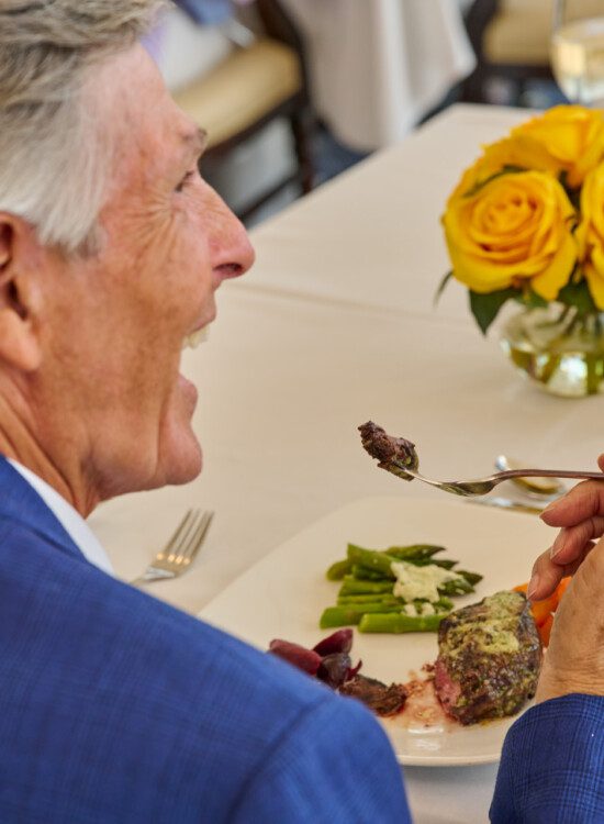 close-up of senior man enjoying a bite of medium rare steak in the upscale dining room at Harbour's Edge Senior Living Community