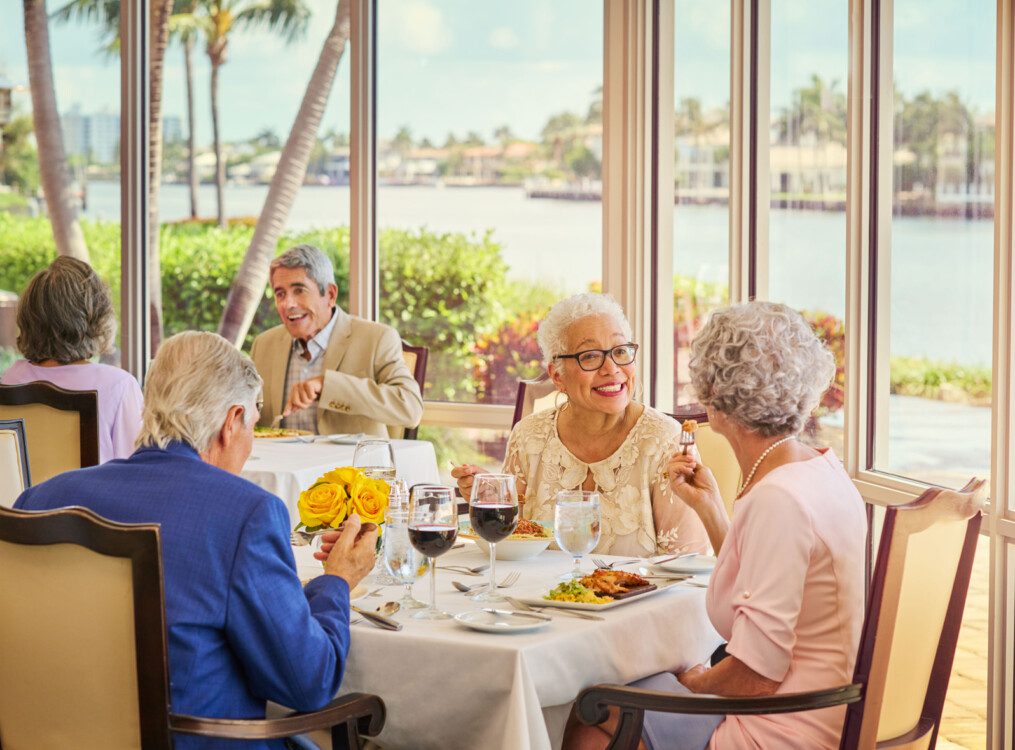 two groups of seniors dine at elegant tables while enjoying wine and chef-prepared meals at Harbour's Edge with panoramic waterfront views