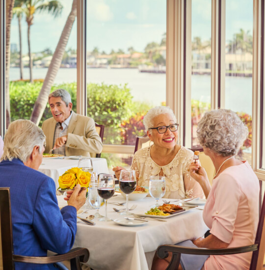 two groups of seniors dine at elegant tables while enjoying wine and chef-prepared meals at Harbour's Edge with panoramic waterfront views