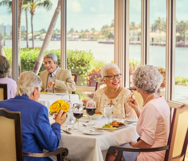 two groups of seniors dine at elegant tables while enjoying wine and chef-prepared meals at Harbour's Edge with panoramic waterfront views