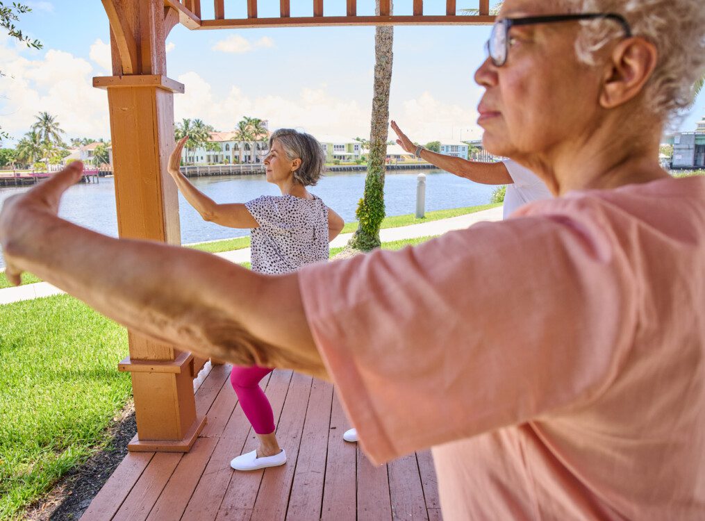 group of three senior women practice Tai Chi in an outdoor gazebo on a sunny day by the water at Harbour's Edge Senior Living Community