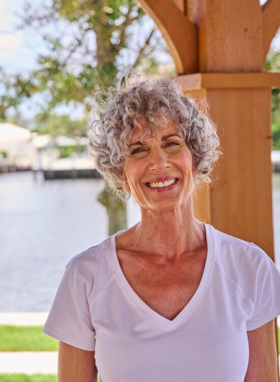 smiling senior woman looks directly at the camera while standing beneath an outdoor gazebo at Harbour's Edge Senior Living Community