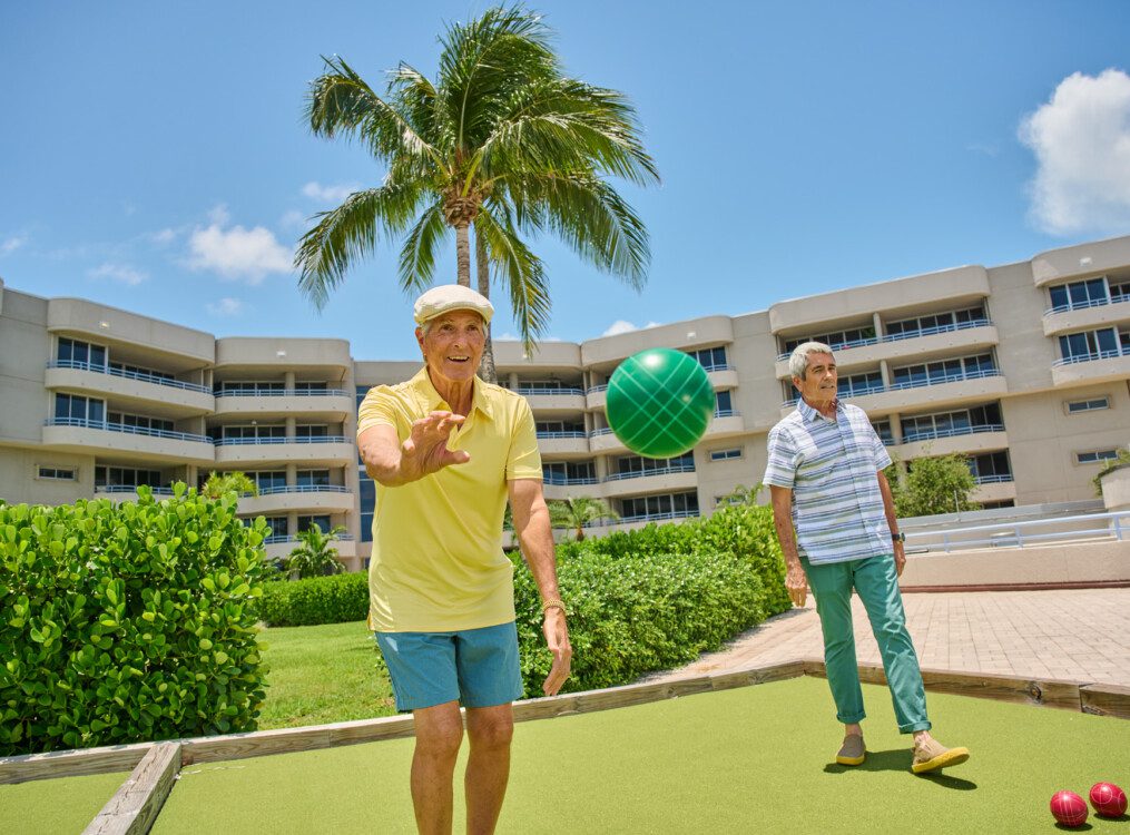 two smiling senior men in casual clothes play bocce ball outdoors at Harbour's Edge Senior Living Community in Delray Beach, FL
