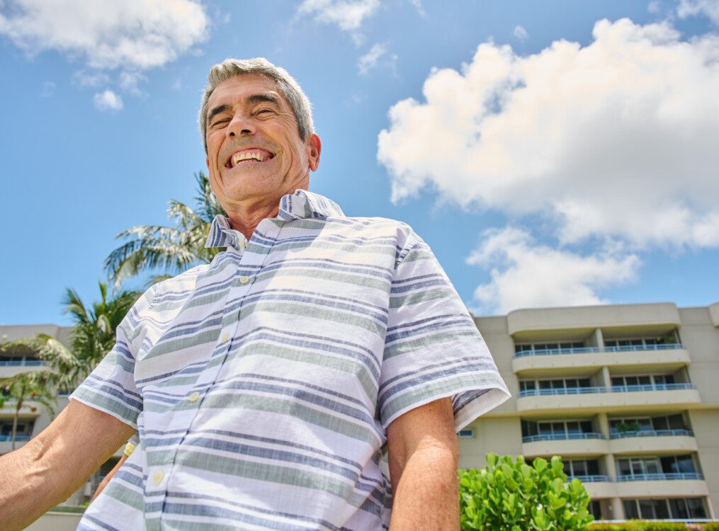 senior man smiles after a game of bocce ball, backdropped by the buildings at Harbour's Edge Senior Living Community
