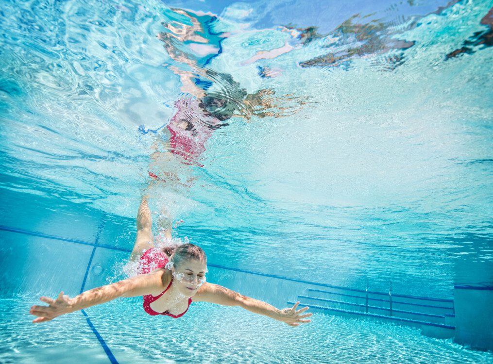 senior woman swims underwater in expansive resort-style pool