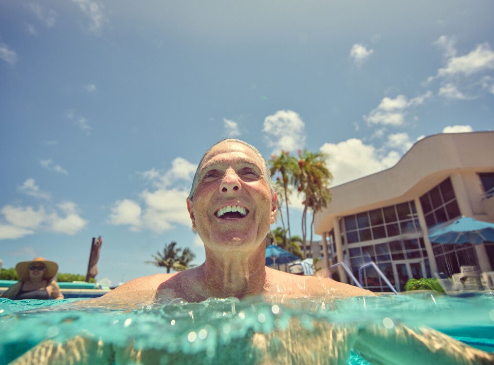 close-up of smiling senior man half-submerged in the waters of the resort pool at Harbour's Edge Senior Living Community