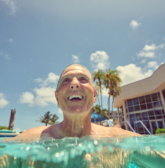 close-up of smiling senior man half-submerged in the waters of the resort pool at Harbour's Edge Senior Living Community