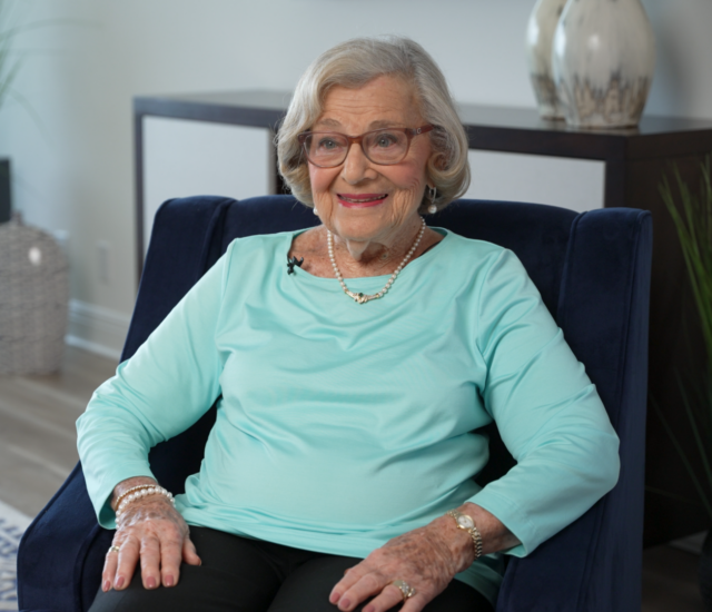 senior woman (Zelda Luxenberg) smiles at person off camera while seated for interview