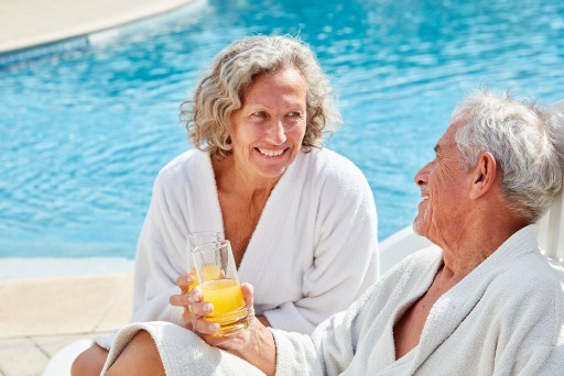 senior couple sitting poolside as they toast with their drinks