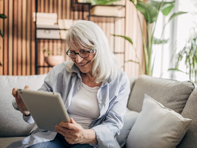 Smiling older adult woman using tablet to communicate with friend.