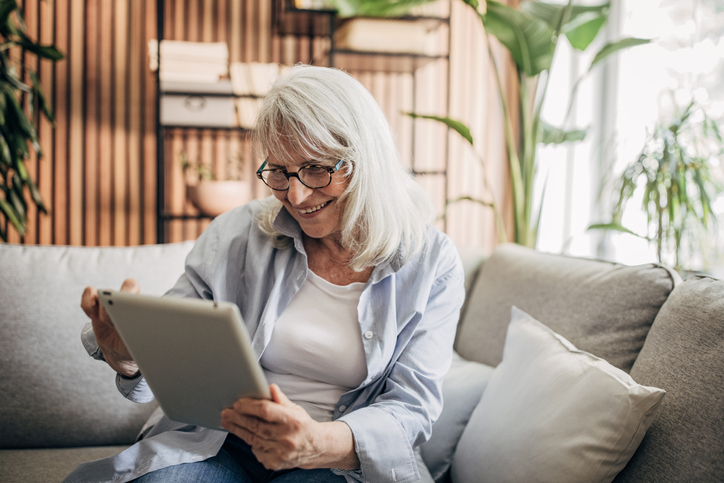 Smiling older adult woman using tablet to communicate with friend.