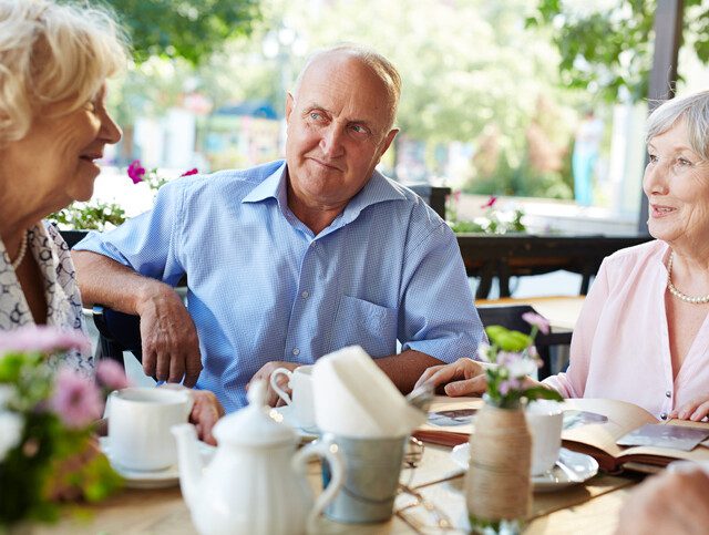 Older adults engaged in conversation around an outdoor table.