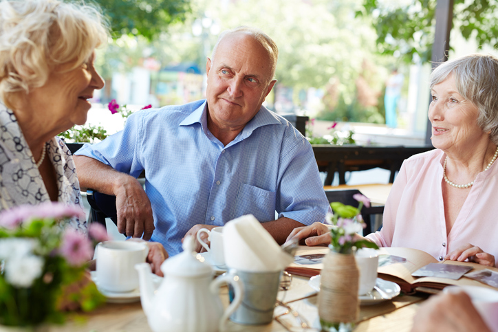 Older adults engaged in conversation around an outdoor table.